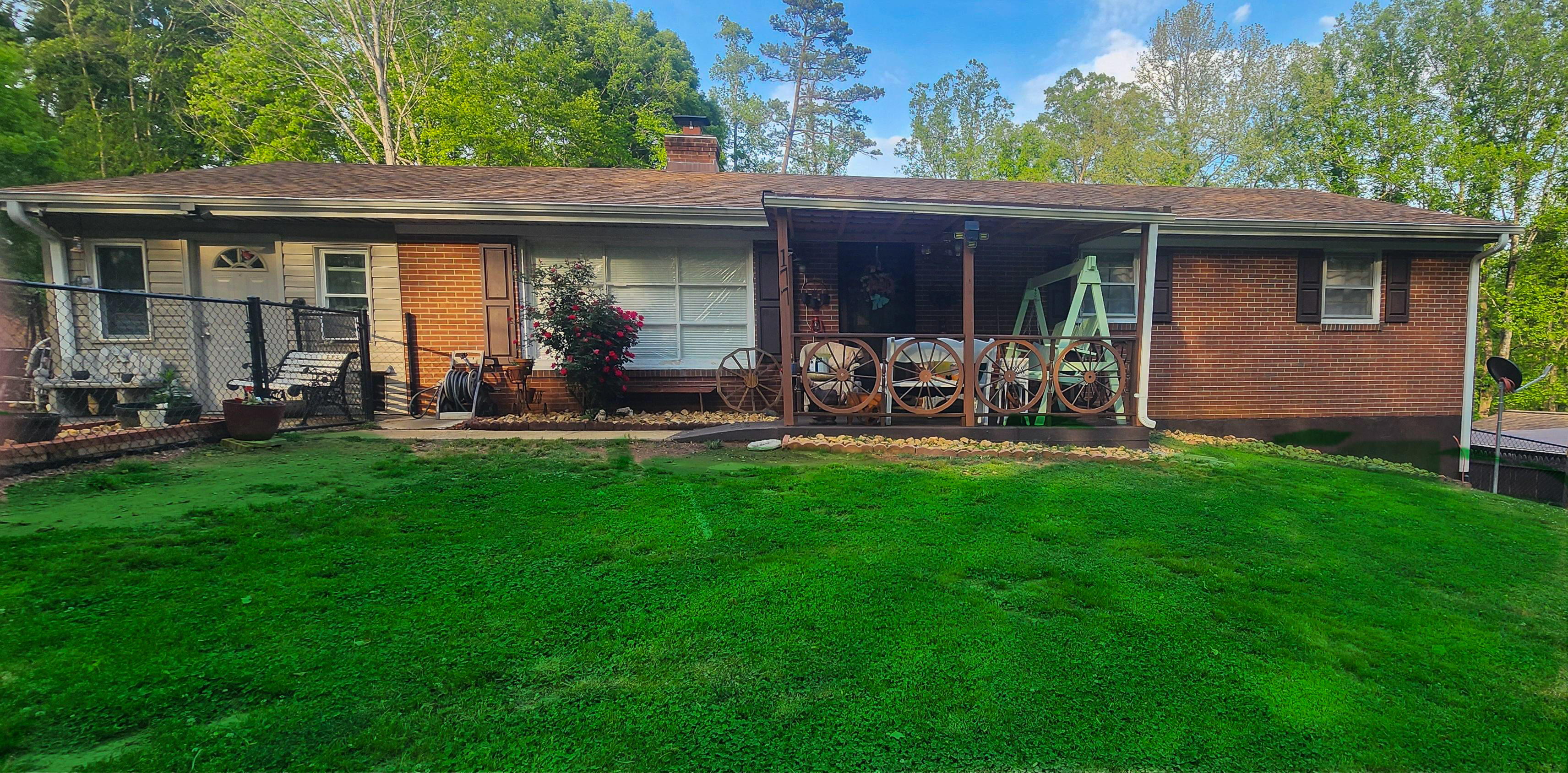Single‑story brick house with a covered porch, outdoor seating, and a large green lawn bordered by trees belonging to Sponsored Residential Provider Cindy Freeman in Bassett, Virginia.