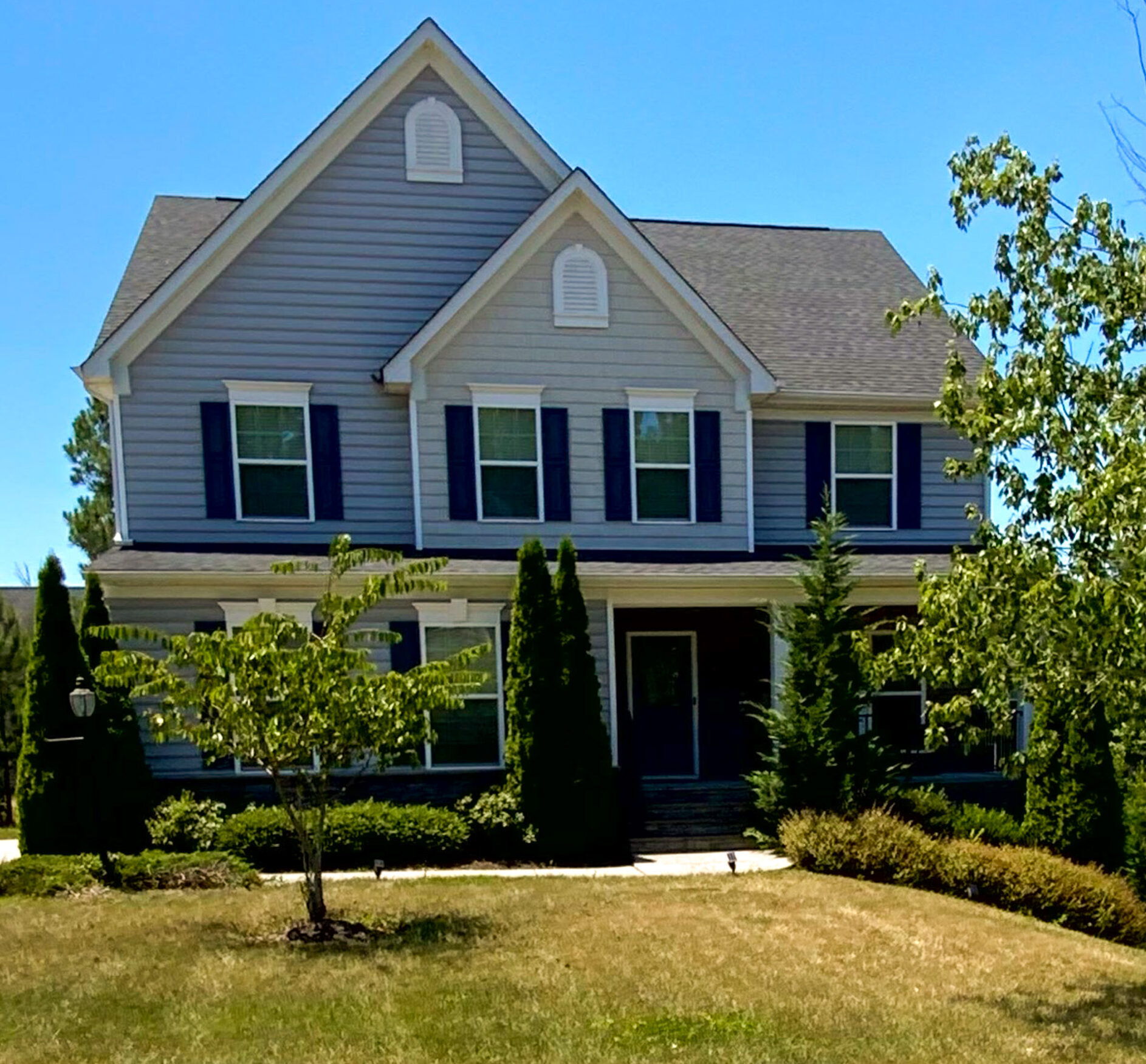A two‑story gray house with dark shutters is framed by tall shrubs and a neatly maintained front yard belonging to Sponsored Residential Provider Derrick Moseley in Richmond, Virginia.
