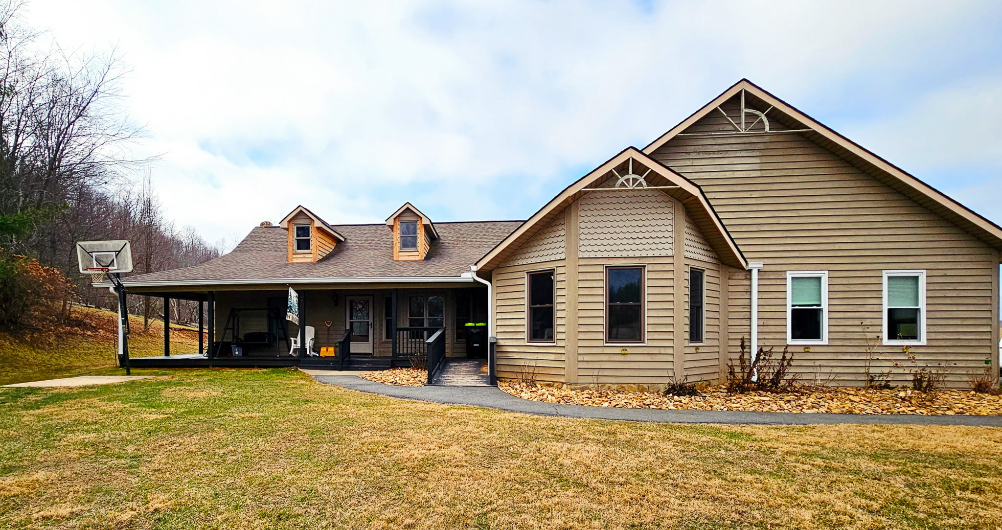 A tan single‑story house with gabled rooflines, dormer windows, a covered side porch, and a curved walkway across a large yard belonging to Group Home Provider Dylan Mays in Woodlawn, Virginia.