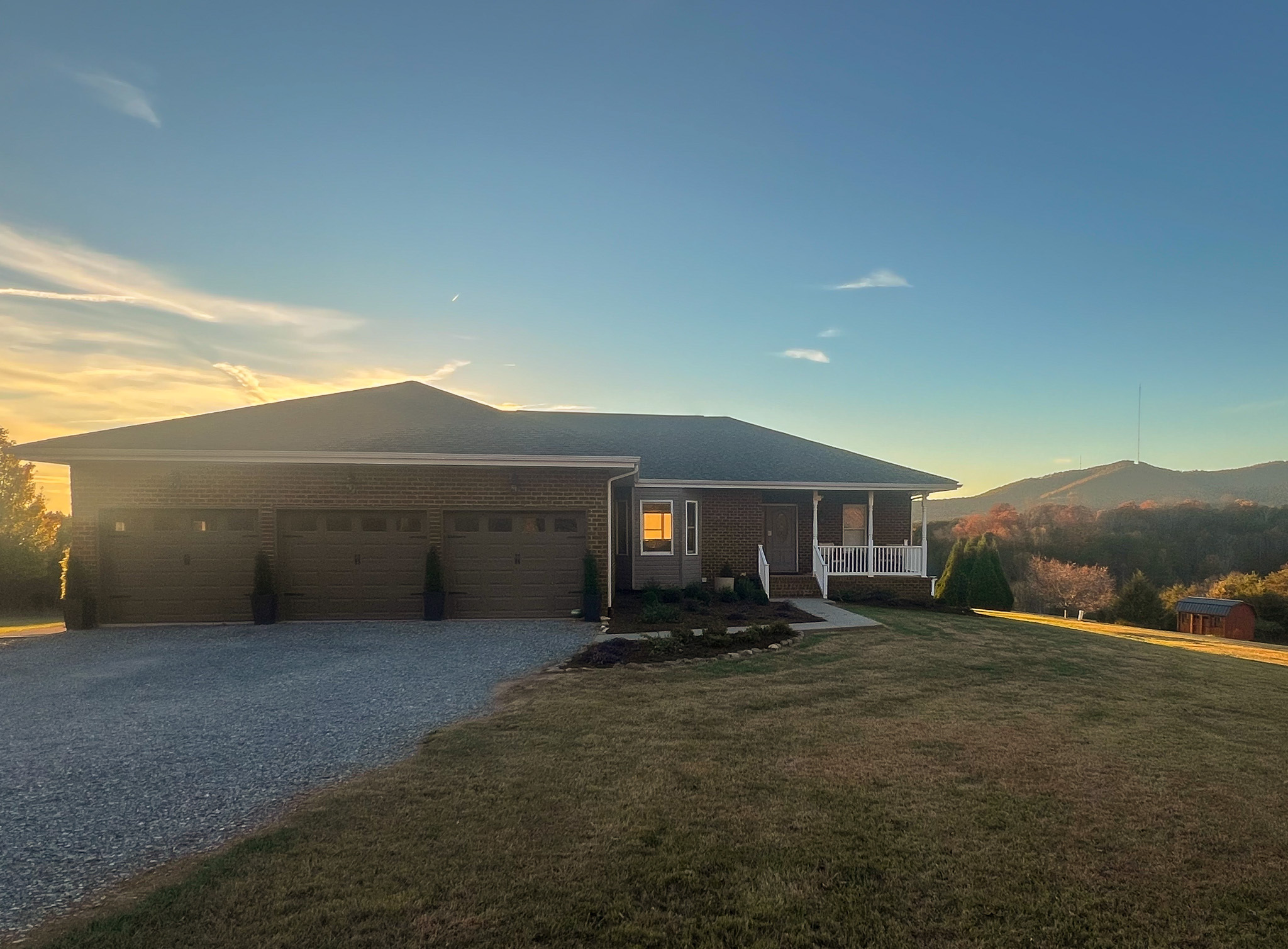 Brick house with a three‑car garage, front porch, and a wide lawn belonging to Sponsored Residential Providers Nathan and Leigh Habecker in Bedford, Virginia at sunset with mountains in the background.