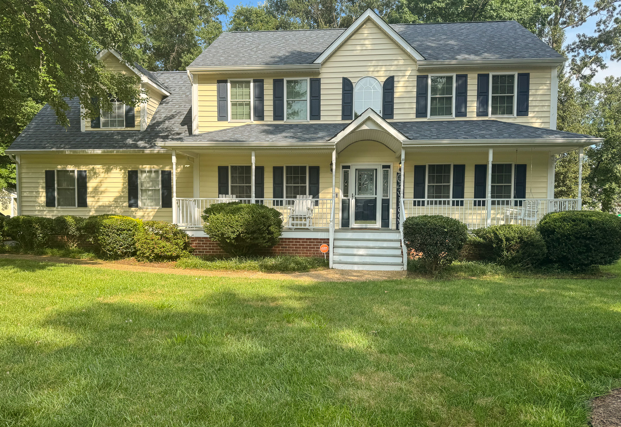 A two‑story yellow house with white trim and a wide front porch is surrounded by neatly maintained shrubs and a large green lawn belonging to Sponsored Residential Provider Durand Holloway in Chester, Virginia.